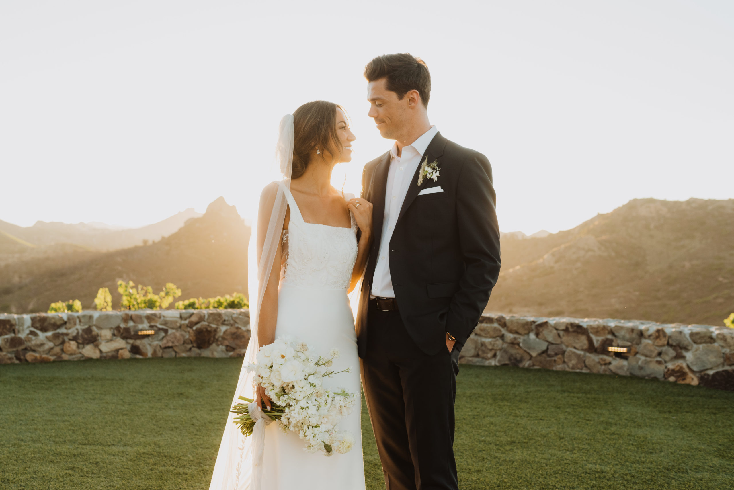 bride and groom are looking at eachother while the sun illuminates them from behind