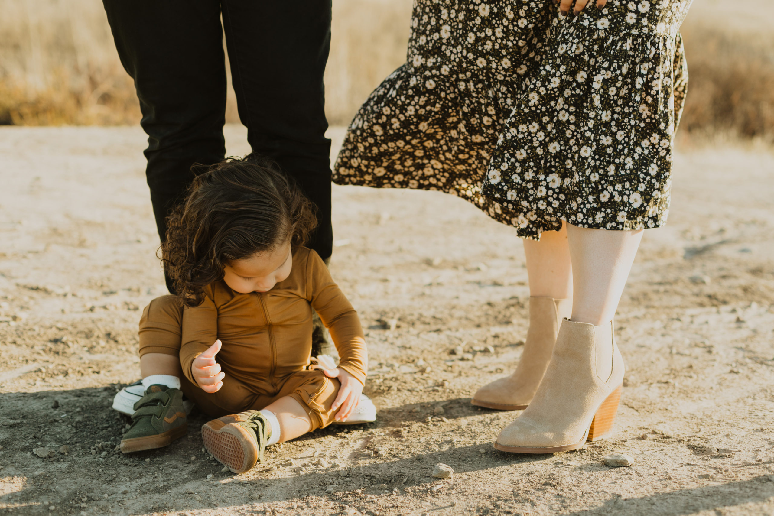 shot focused on baby sitting on the ground next to parents feet